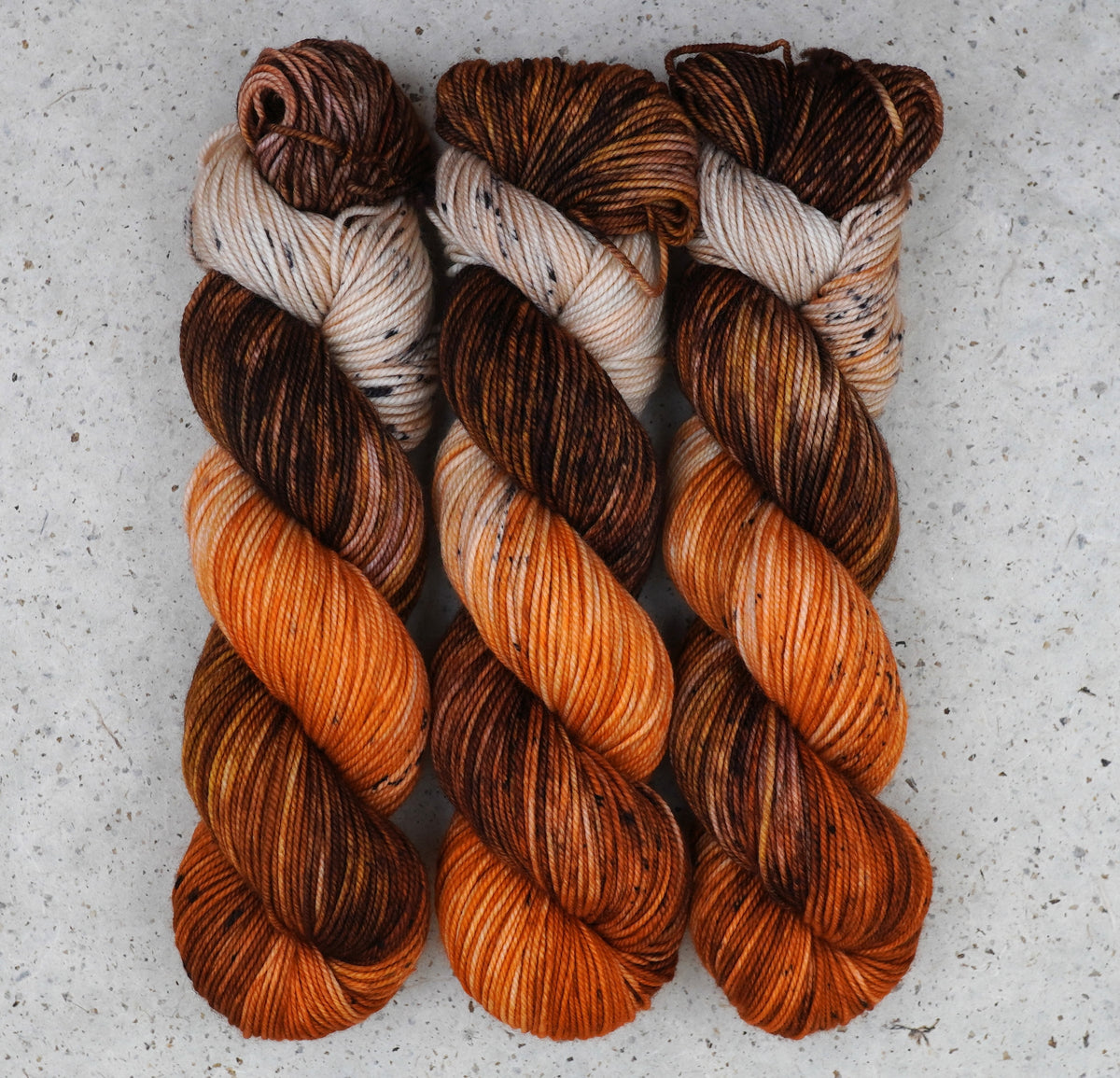 Wild Woollys Autumn Mocha DK yarn, three skeins in brown, orange, and cream with dark speckles