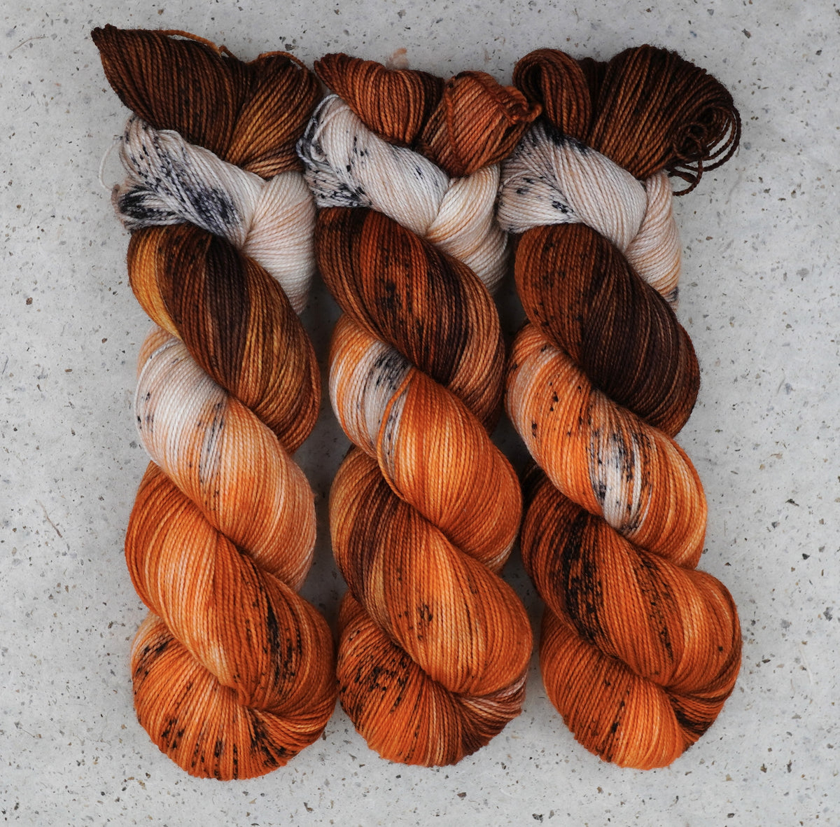 Wild Woollys Autumn Mocha Fingering yarn, three skeins in brown, orange, and cream with dark speckles
