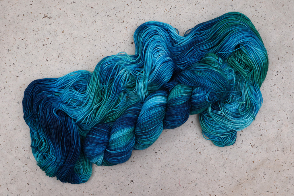 Wild Woollys Cerulean Rhapsody yarn, an unwound skein showing teal, turquoise, and deep blue