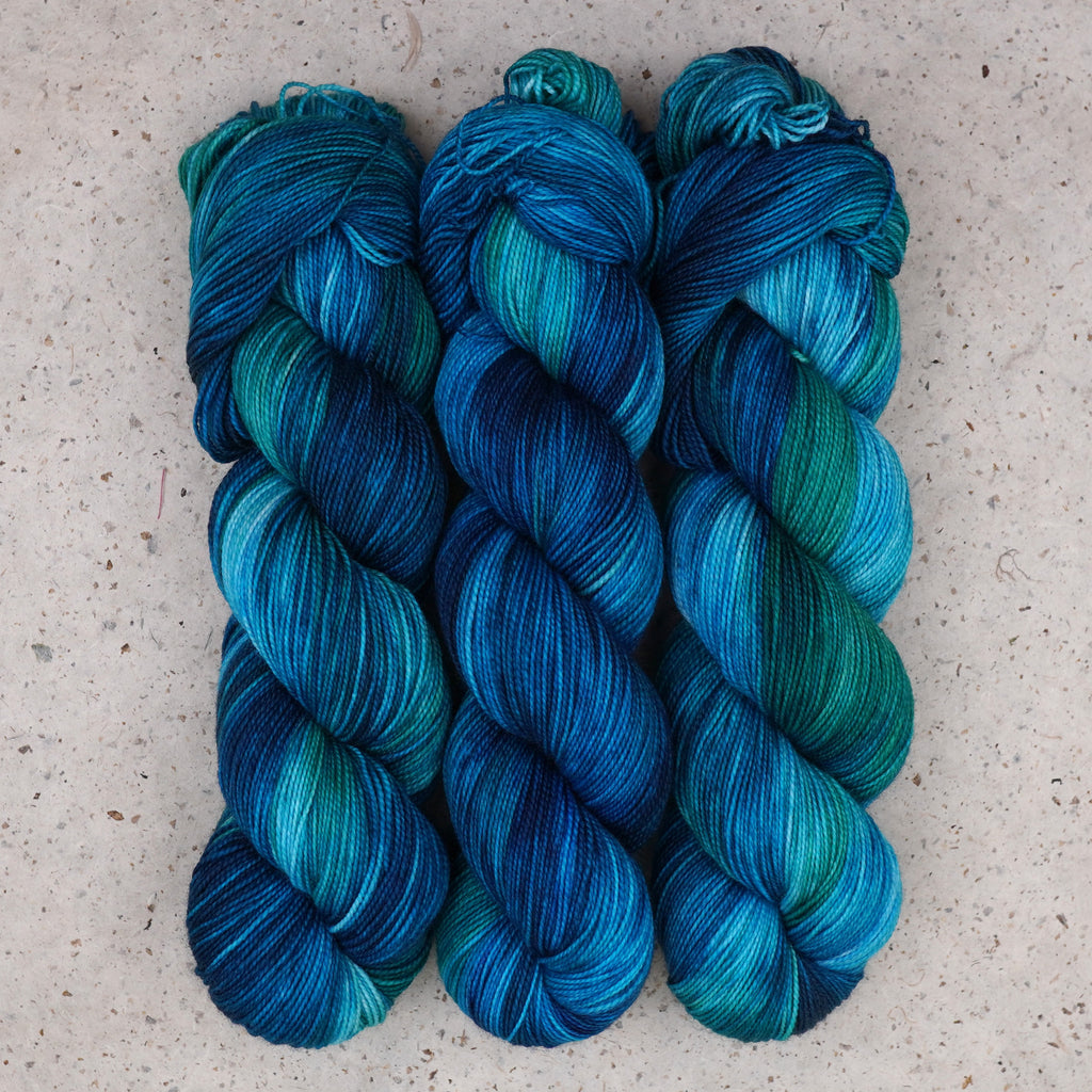 Wild Woollys Cerulean Rhapsody Fingering yarn, three skeins in teal, turquoise, and deep blue