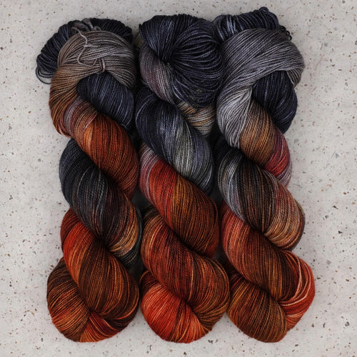 Hilo Fingering Cobalt Rust de Wild Woollys, tres madejas en gris antracita, azul pizarra y naranja óxido