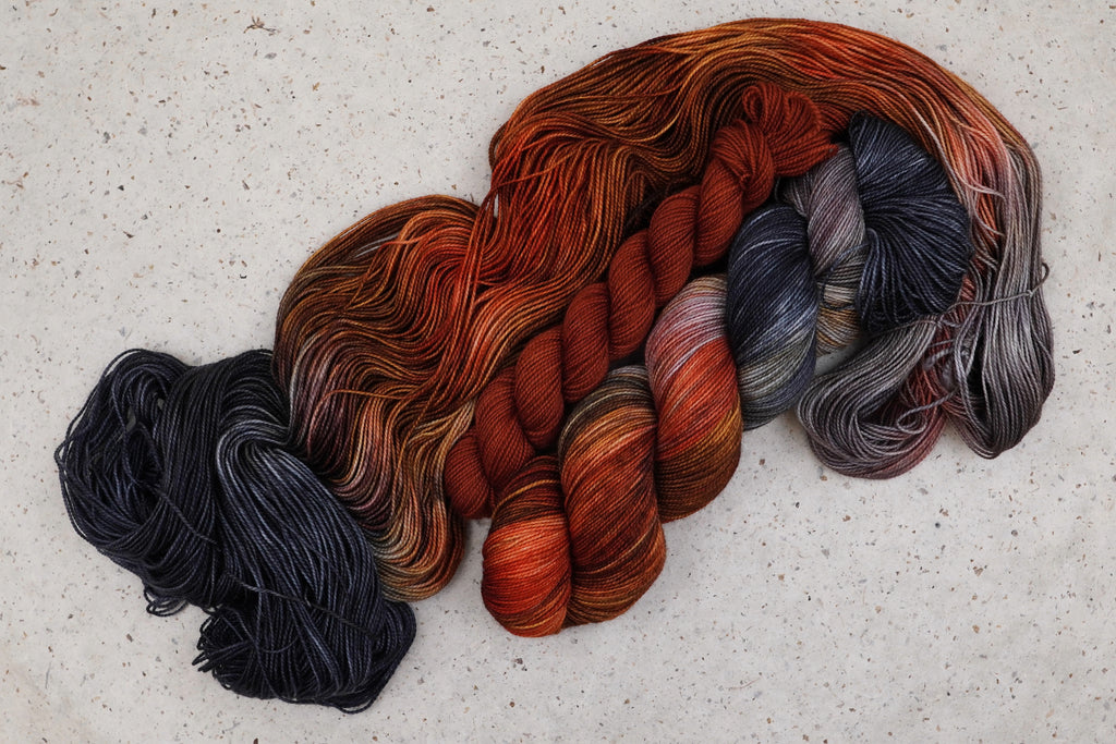 Kit chaussettes Cobalt Rust de Wild Woollys : écheveaux ouverts aux tons orange rouille, gris anthracite et gris acier, avec un mini-écheveau contrastant orange rouille