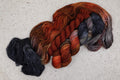 Kit chaussettes Cobalt Rust de Wild Woollys : écheveaux ouverts aux tons orange rouille, gris anthracite et gris acier, avec un mini-écheveau contrastant orange rouille