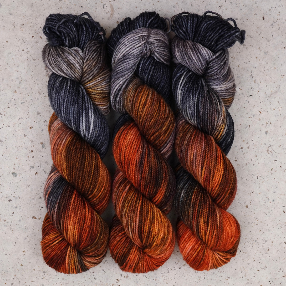 Wild Woollys Cobalt Rust DK yarn, three skeins in charcoal grey, slate blue, and rust orange