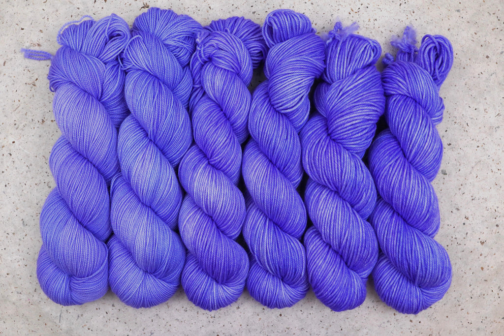 Six skeins of Wild Woollys Crocus Pocus lined up in a row, in periwinkle and violet purple