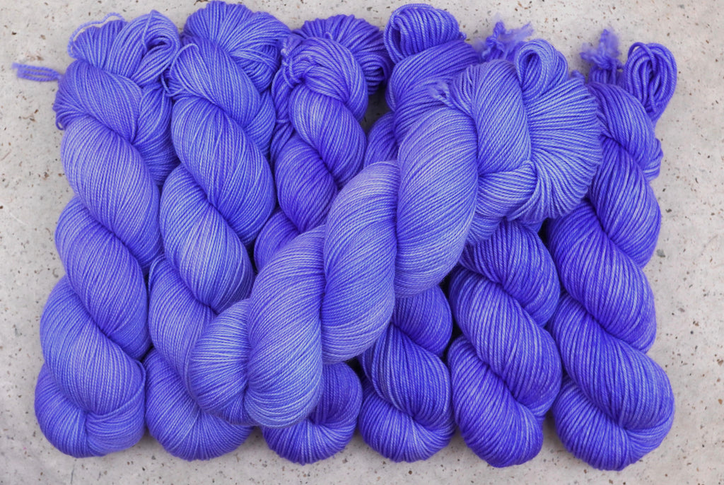 Six skeins of Wild Woollys Crocus Pocus lined up in a row, in periwinkle and violet purple