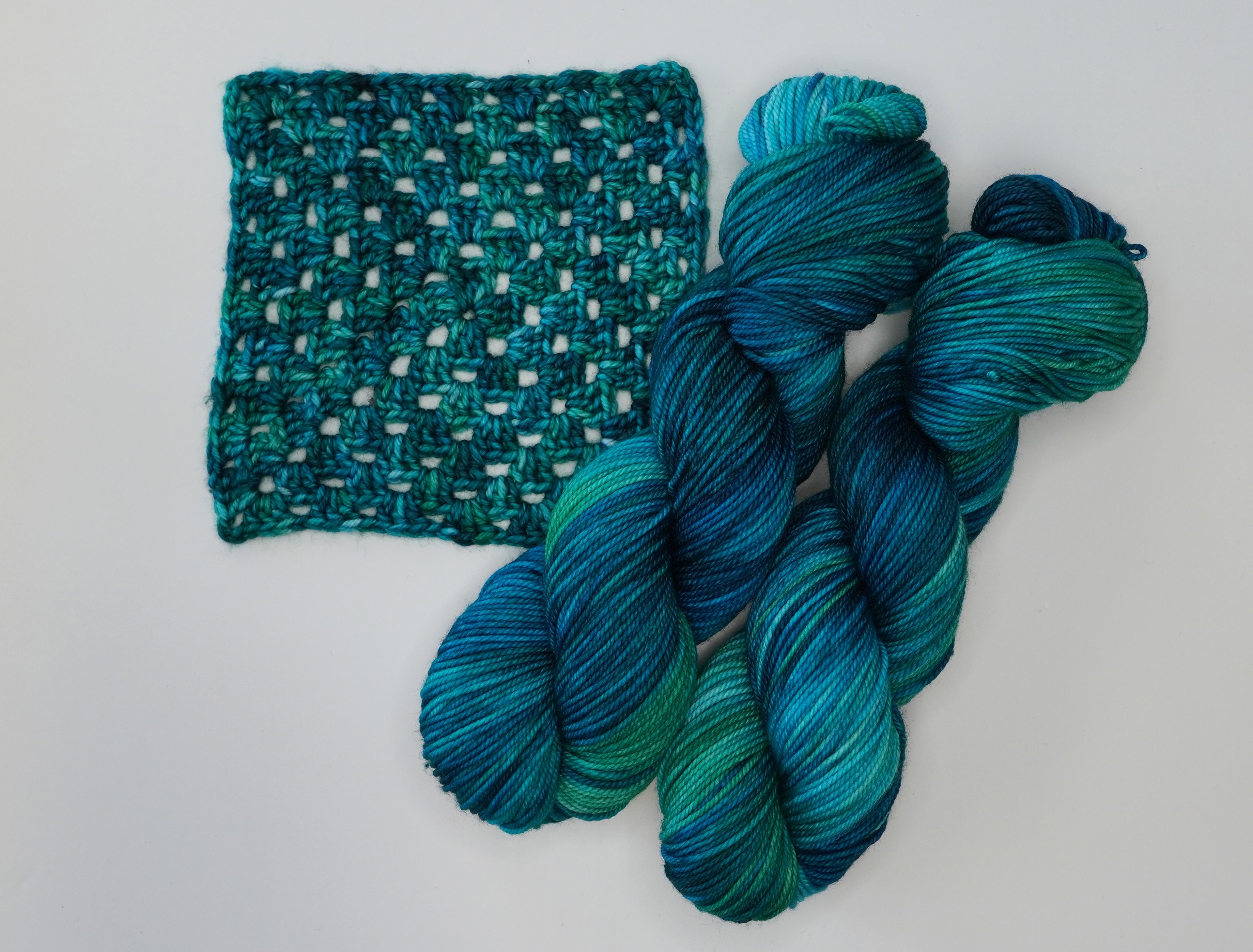 Cerulean Rhapsody yarn by Wild Woollys, two skeins and a crocheted swatch in shades of blue and green