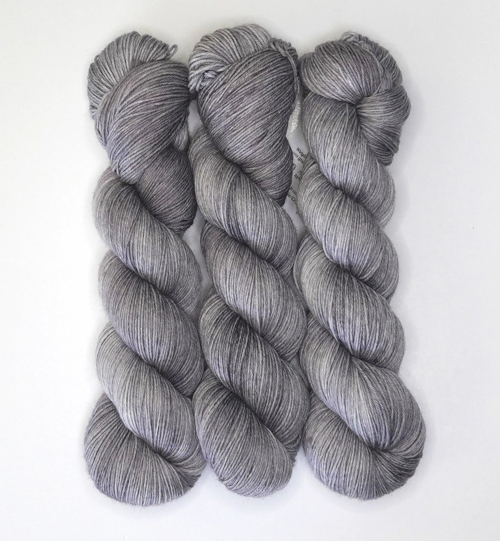 Three skeins of Wild Woollys Grey Expectations yarn in varying shades of grey