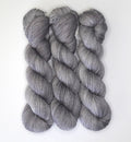 Three skeins of Wild Woollys Grey Expectations yarn in varying shades of grey