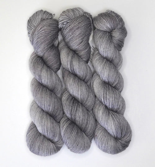 Three skeins of Wild Woollys Grey Expectations yarn in varying shades of grey