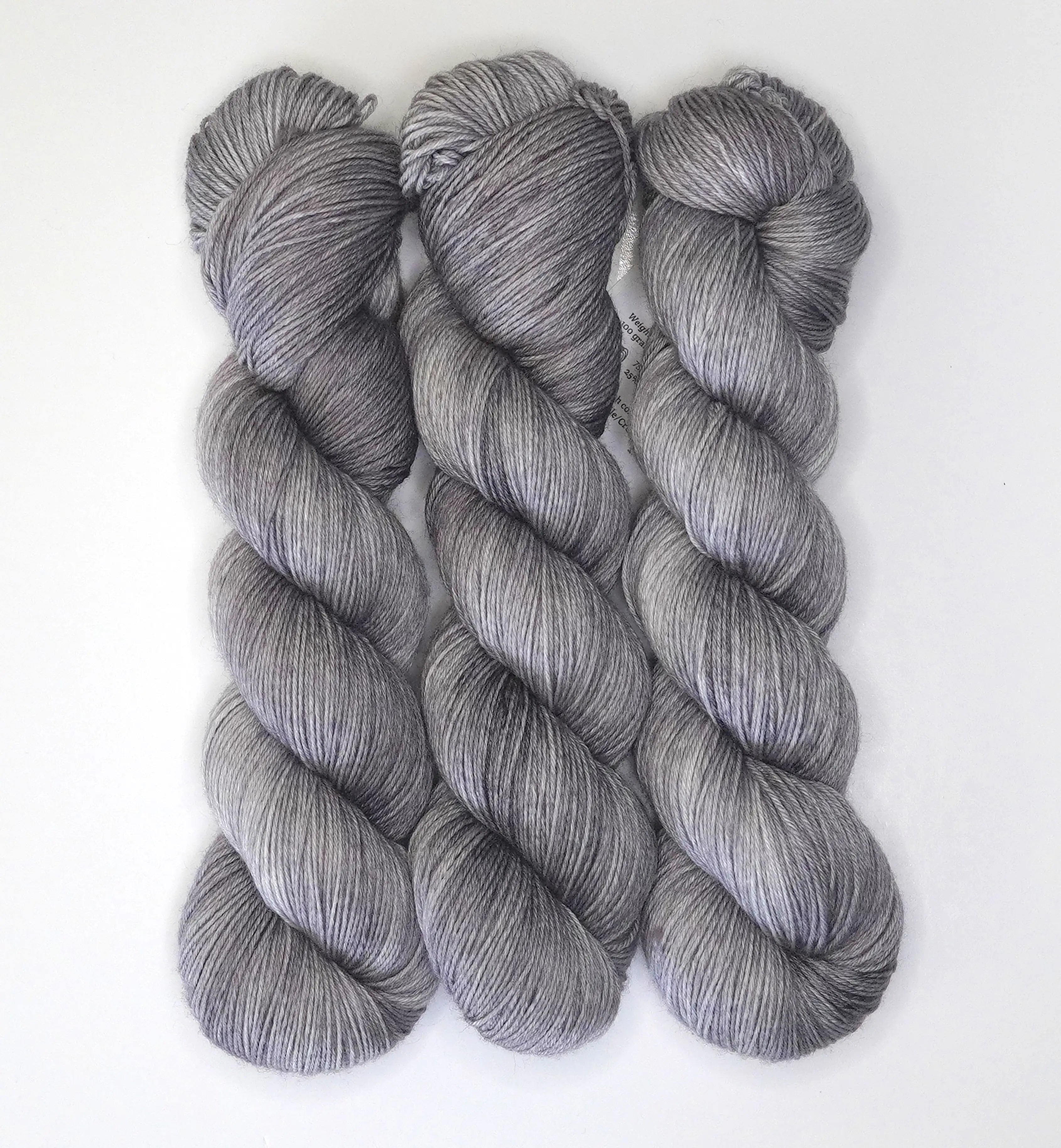 Three skeins of Wild Woollys Grey Expectations yarn in varying shades of grey