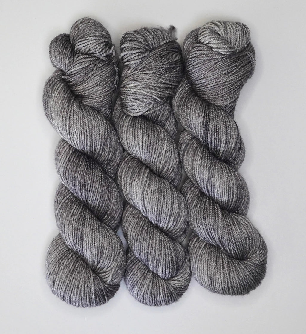 Three skeins of Wild Woollys Grey Expectations yarn in varying shades of grey