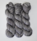 Three skeins of Wild Woollys Grey Expectations yarn in varying shades of grey