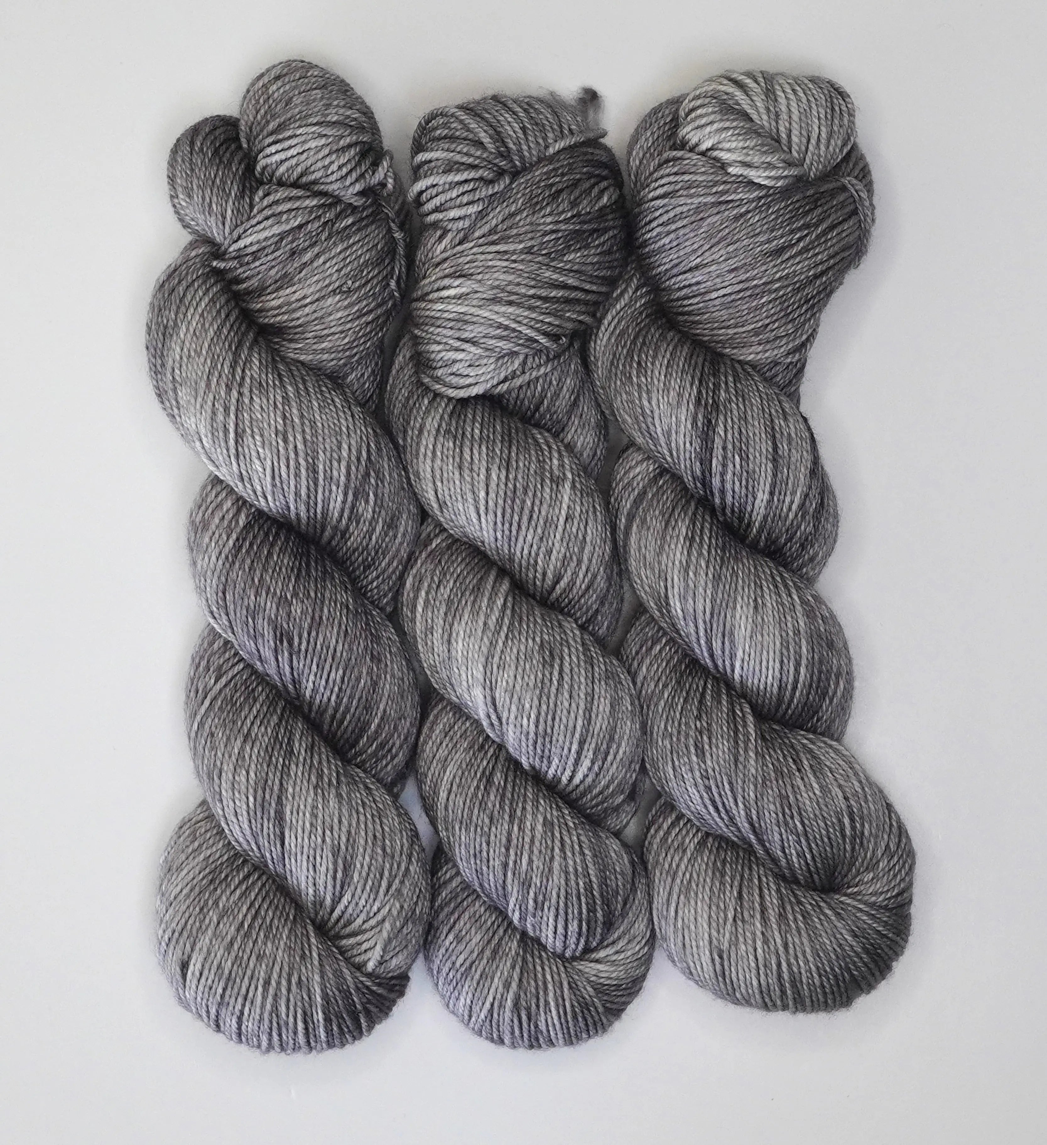 Three skeins of Wild Woollys Grey Expectations yarn in varying shades of grey