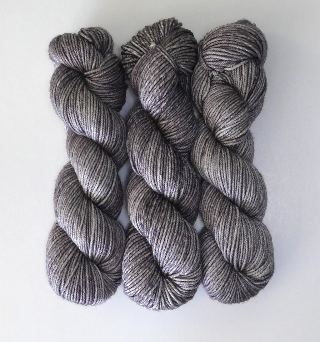 Three skeins of Wild Woollys Grey Expectations yarn, a variegated grey with hints of purple