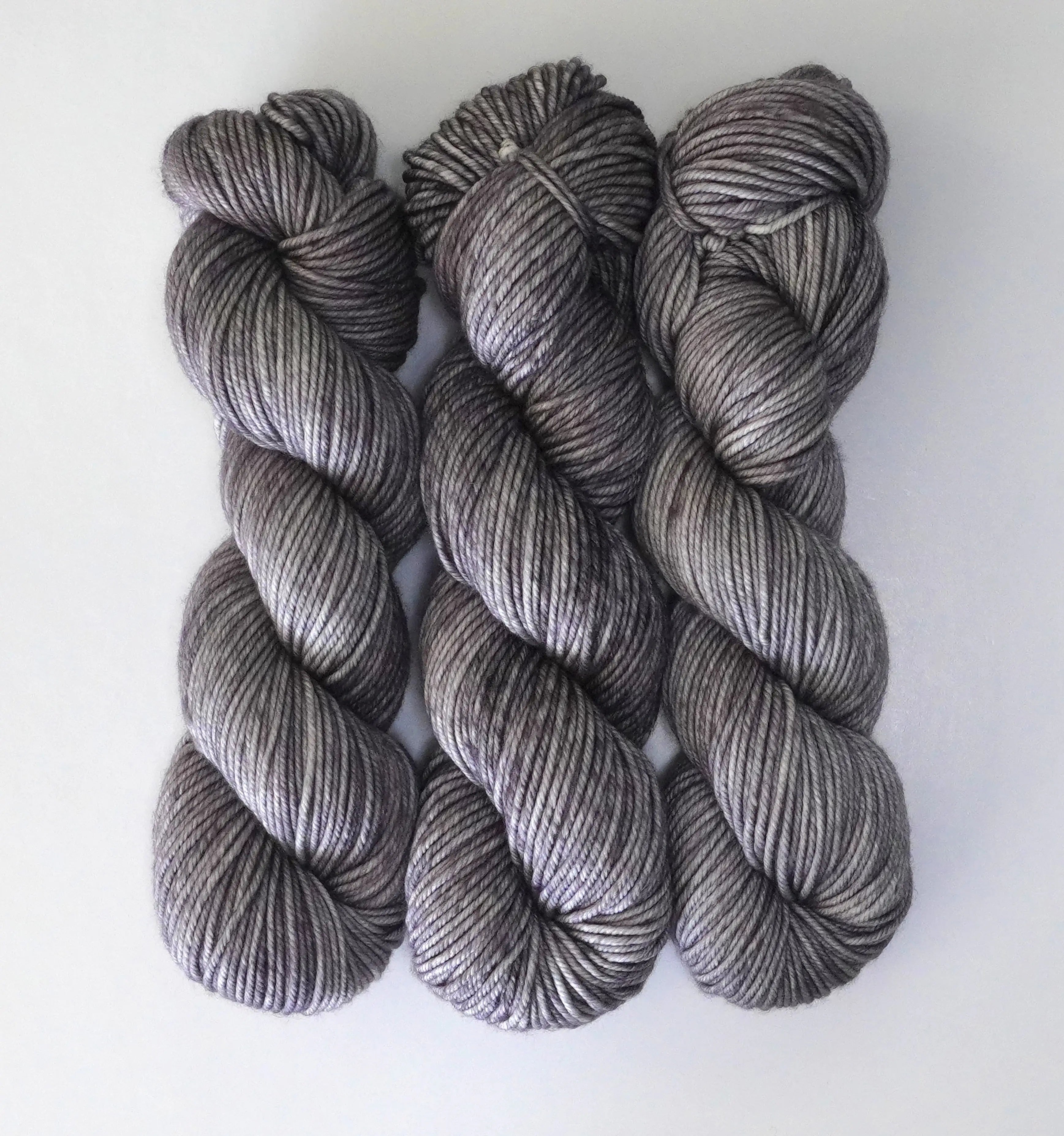 Three skeins of Wild Woollys Grey Expectations yarn, a variegated grey with hints of purple