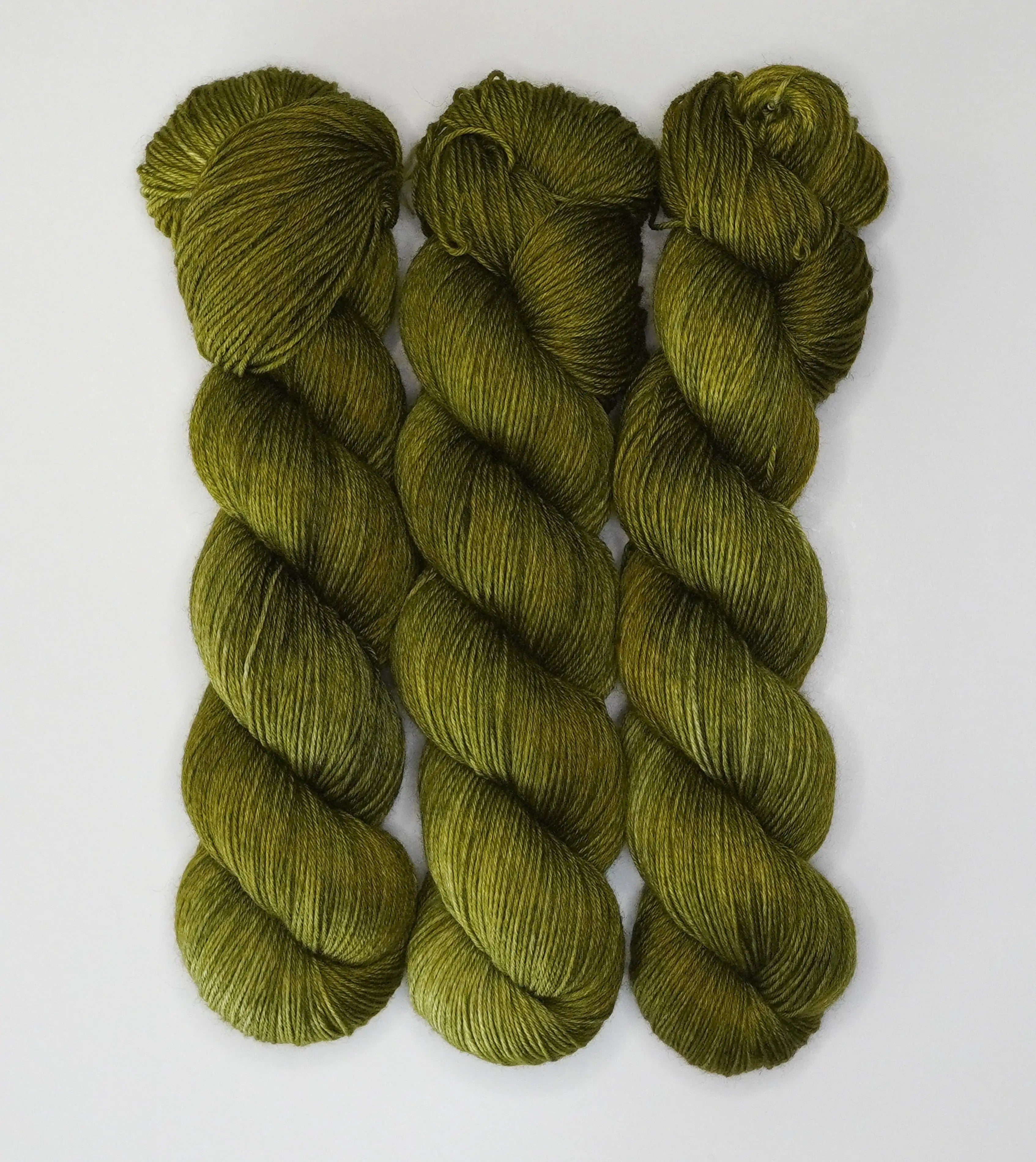 Three skeins of Wild Woollys Fiddlehead Fern yarn, a deep olive green color, on a white background