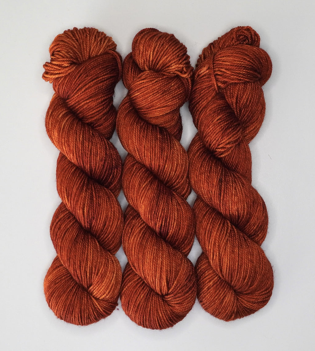Three skeins of Wild Woollys Penny Laine yarn in a rich, variegated rust color