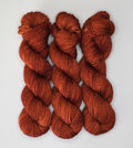 Three skeins of Wild Woollys Penny Laine yarn in a rich, variegated rust color