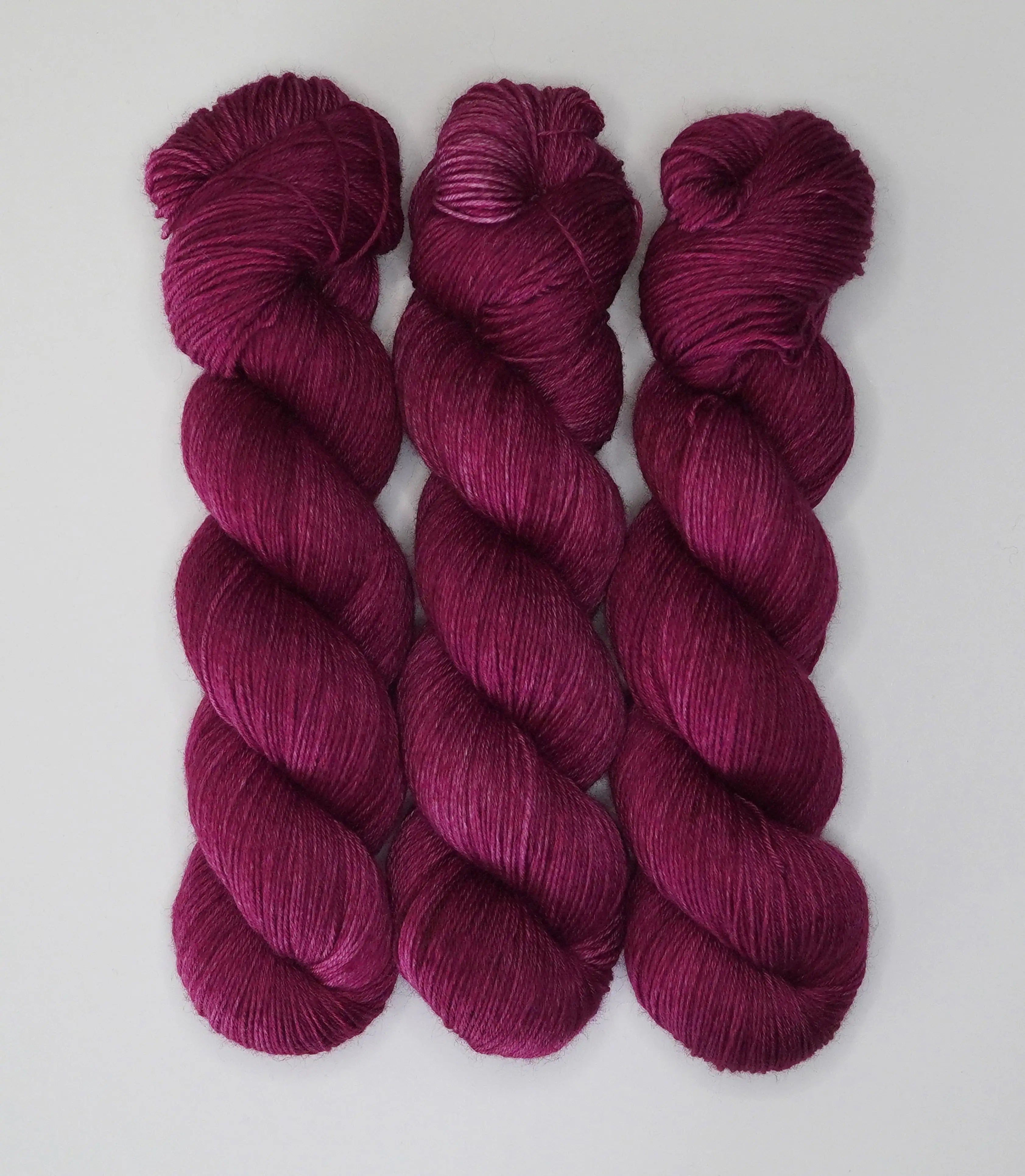 Three skeins of Wild Woollys Fuchsia Nostalgia yarn in a deep magenta color
