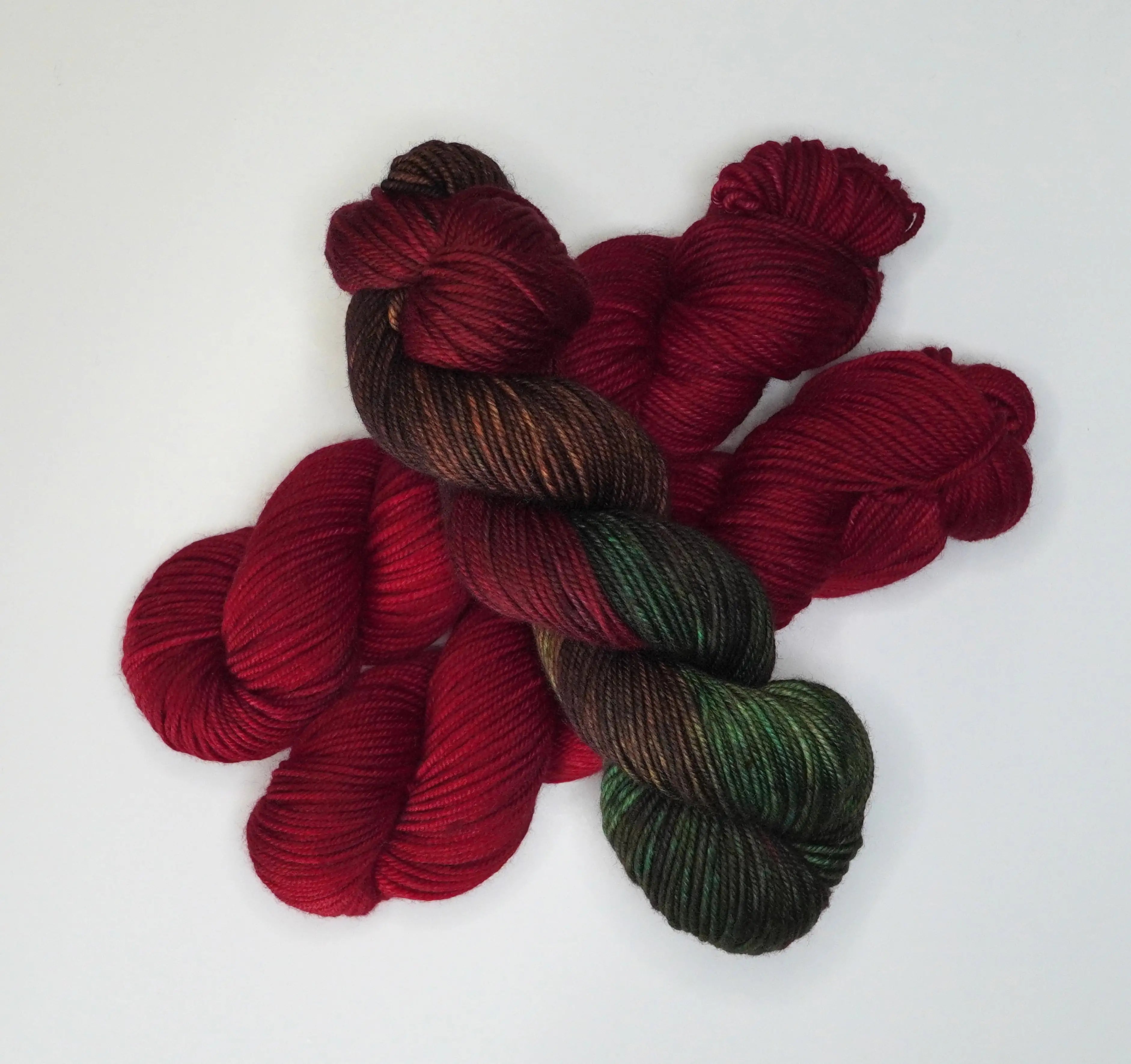 Wild Woollys Divine Wine yarn, a skein of variegated brown and green yarn with three skeins of red yarn
