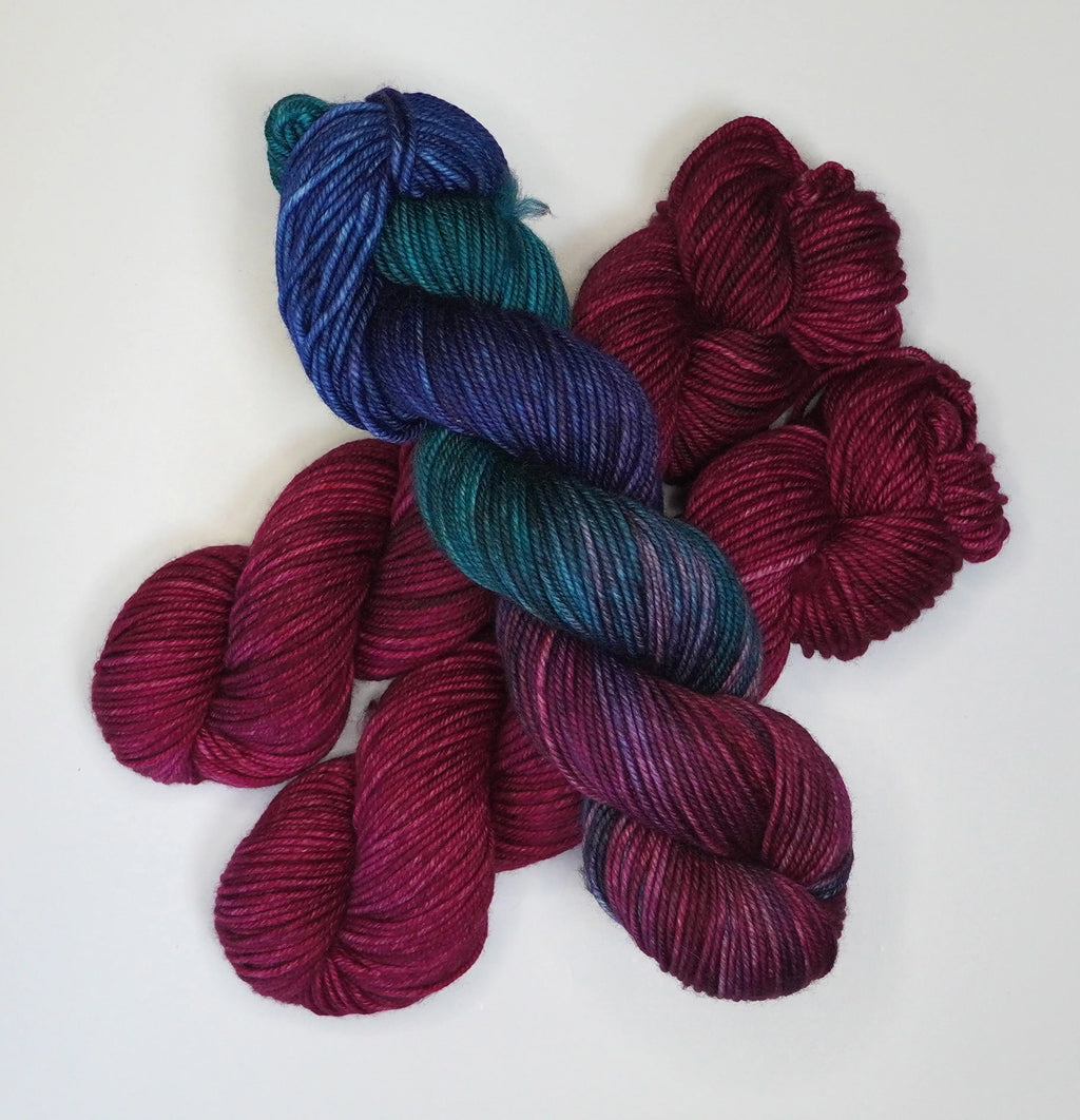 Wild Woollys Fuchsia Nostalgia yarn, one skein variegated blue, teal, and purple, two skeins solid fuchsia