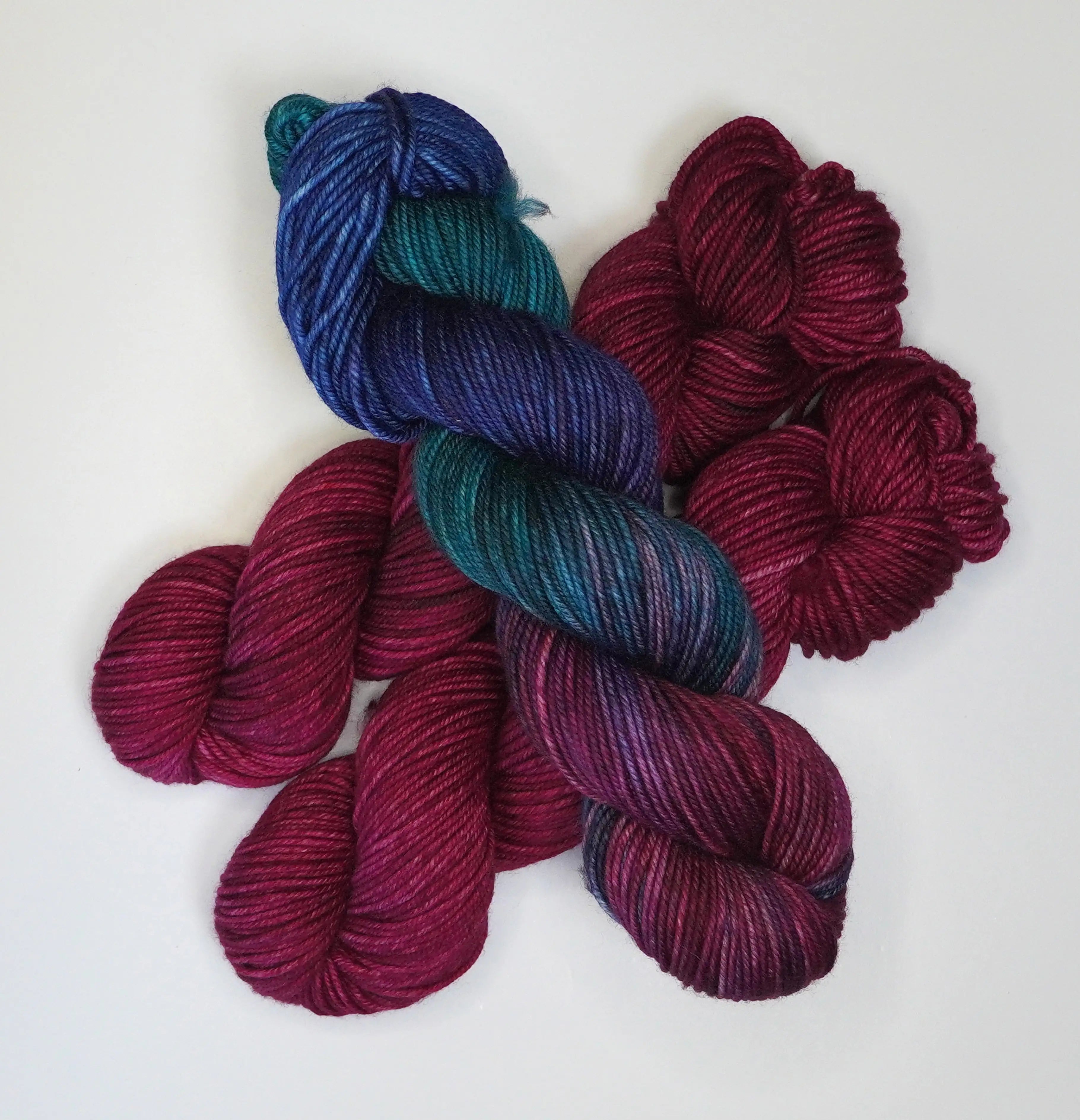 Wild Woollys Fuchsia Nostalgia yarn, one skein variegated blue, teal, and purple, two skeins solid fuchsia