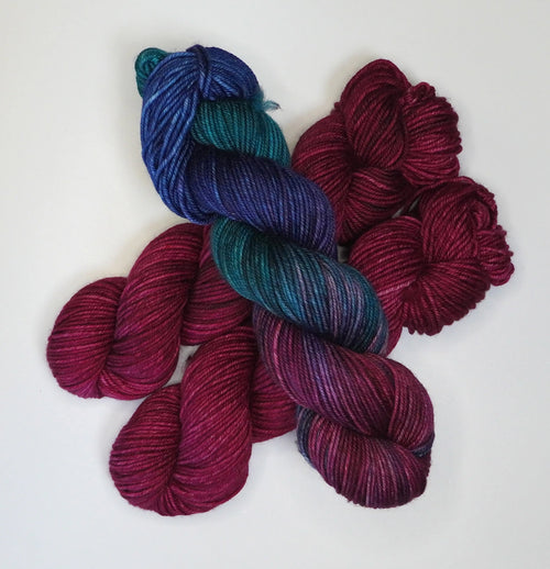 Wild Woollys Fuchsia Nostalgia yarn, one skein variegated blue, teal, and purple, two skeins solid fuchsia