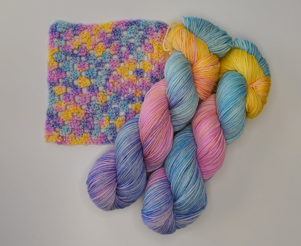 Wild Woollys Fantasy yarn in skeins and a crocheted swatch, featuring blue, pink, purple, and yellow