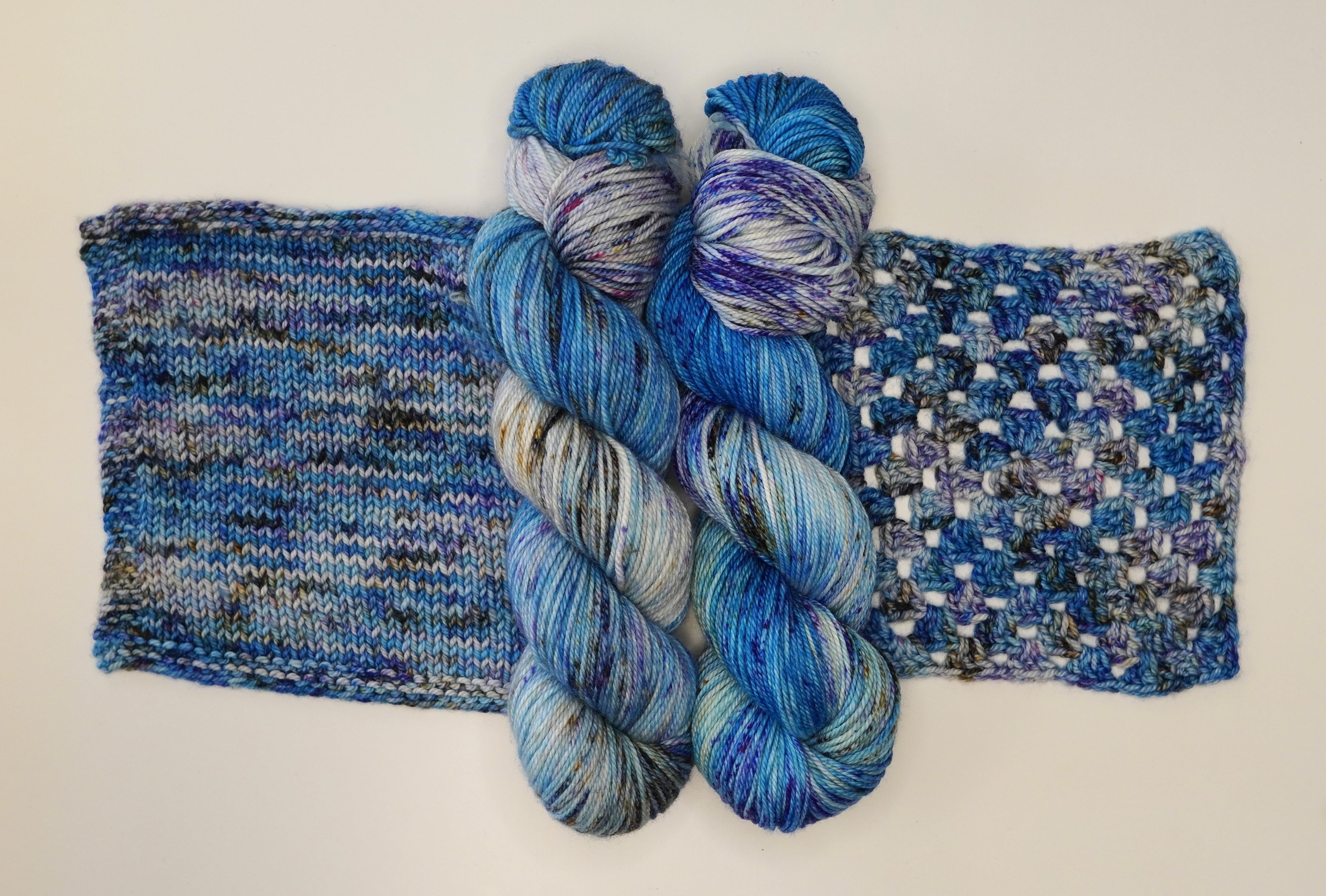 Wild Woollys Galaxy Voyage yarn in two skeins and two knitted swatches, blue, purple, and white