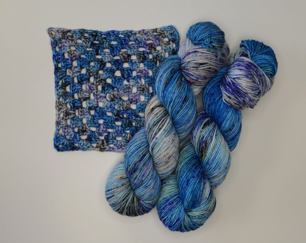 Wild Woollys Galaxy Voyage yarn with a crocheted swatch in blues, purples, and grays
