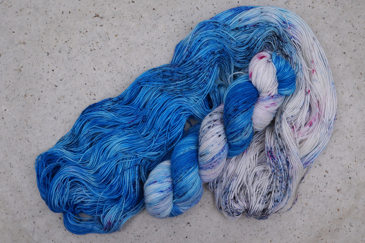 Hilo Galaxy Voyage de Wild Woollys — una madeja abierta en azul brillante y blanco con motas oscuras