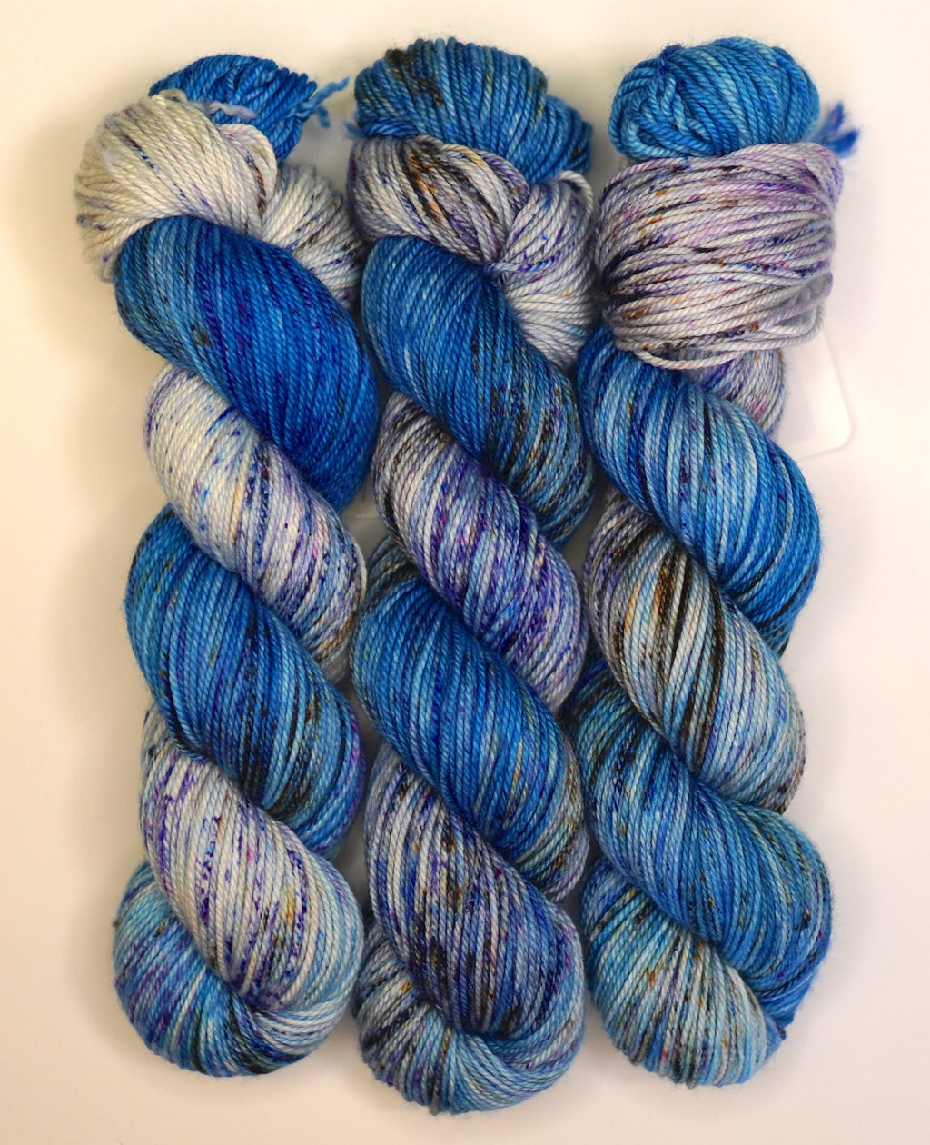 Wild Woollys Galaxy Voyage yarn in three skeins, blue, purple, and white with speckles
