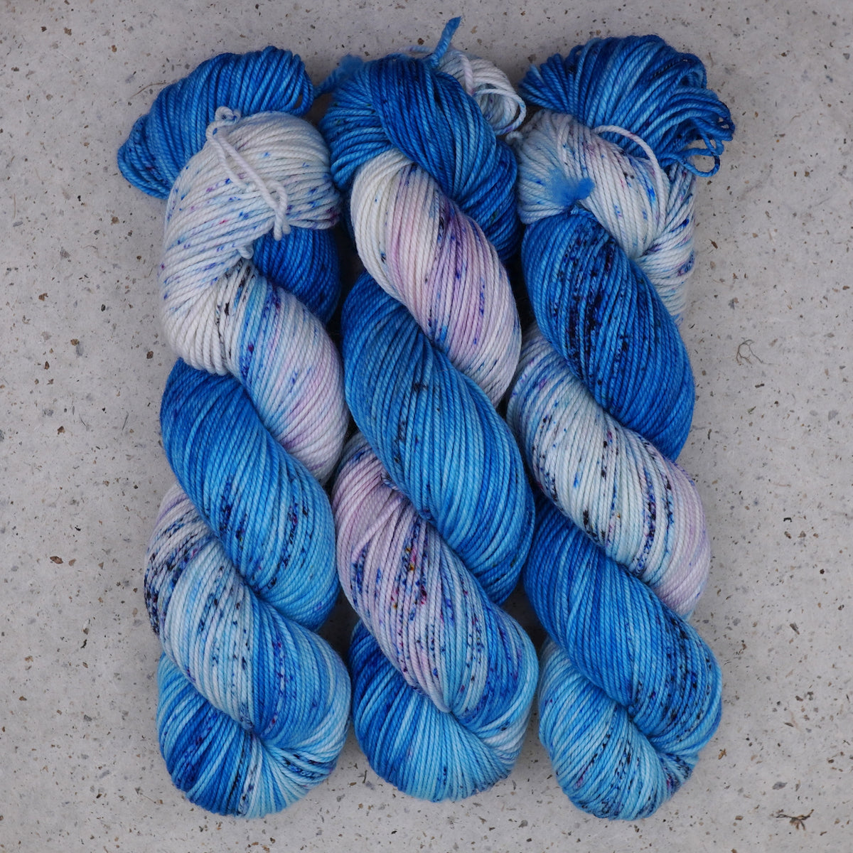 Hilo Galaxy Voyage DK de Wild Woollys — tres madejas en azul brillante y blanco con motas oscuras