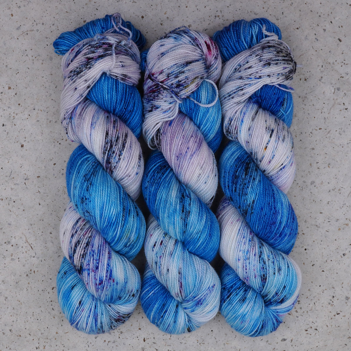 Hilo Galaxy Voyage Fingering de Wild Woollys — tres madejas en azul brillante y blanco con motas oscuras