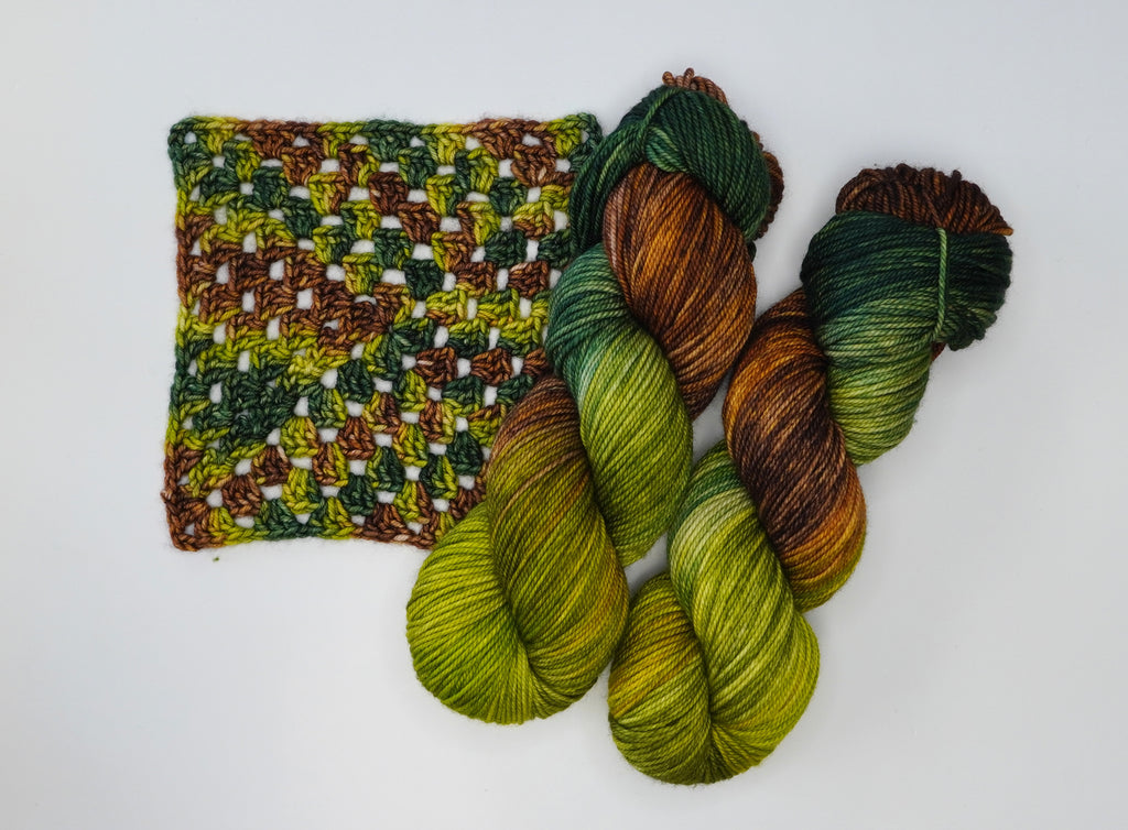 Wild Woollys Jungle Juice yarn with green, brown, and yellow hues, next to a crocheted swatch