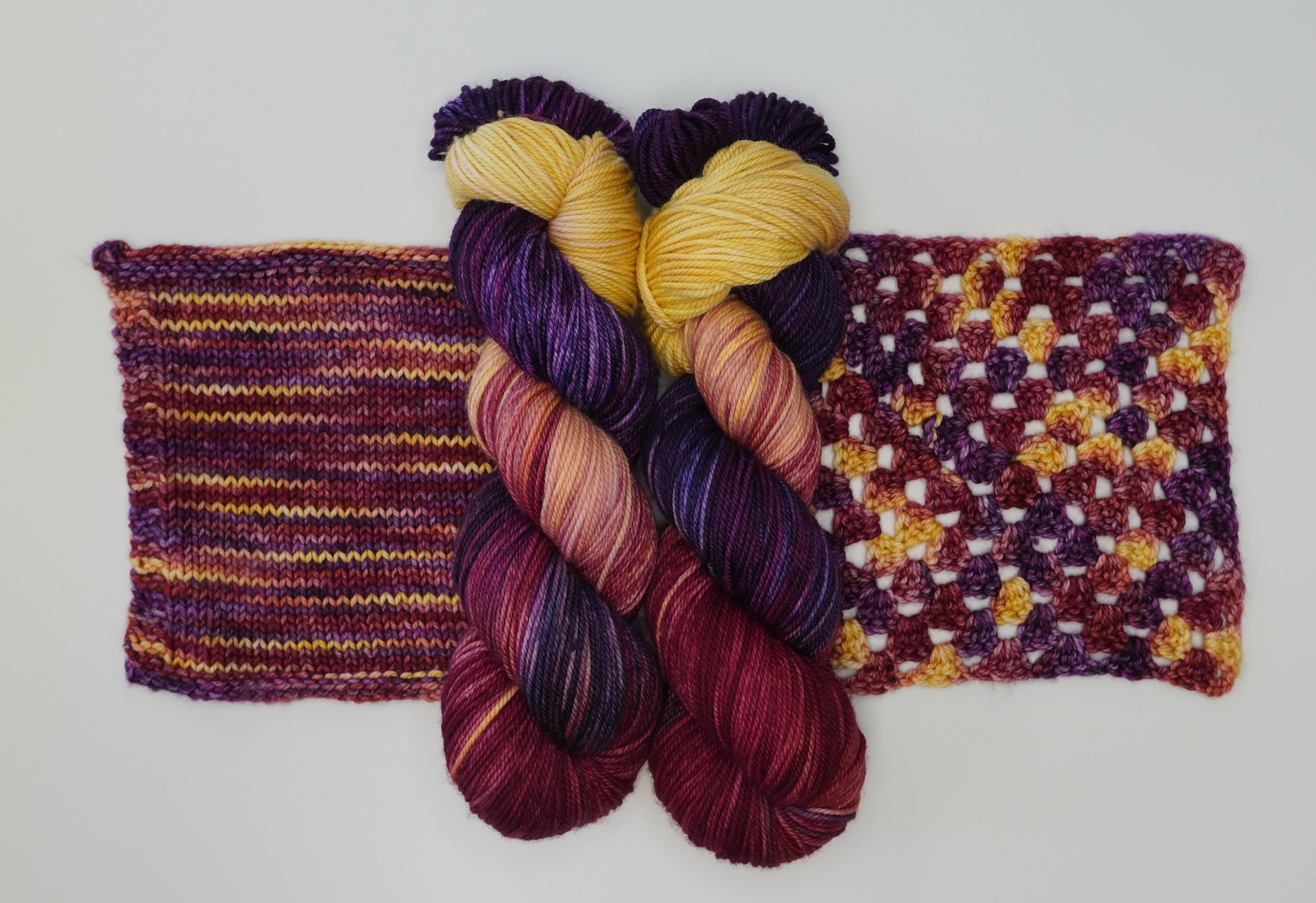 Maizie Dayz yarn by Wild Woollys, two skeins and two swatches, in shades of yellow, purple, and red