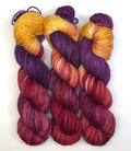 Three skeins of yarn in purple and orange gradient on a white background