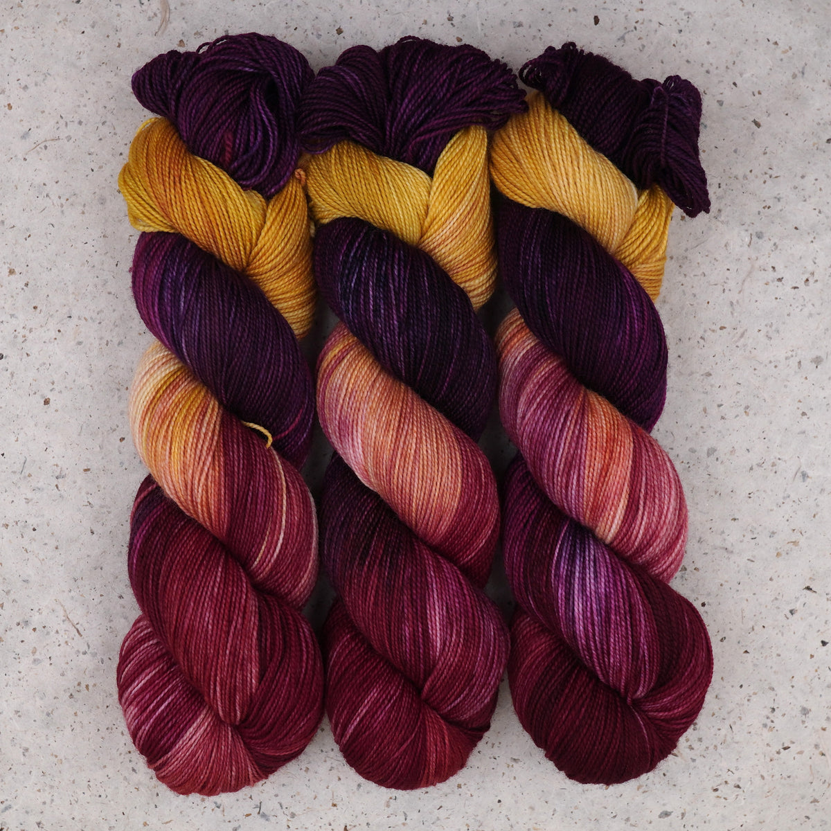 Hilo Maizie Dayz Fingering de Wild Woollys — tres madejas en morado intenso, dorado, magenta y carmesí