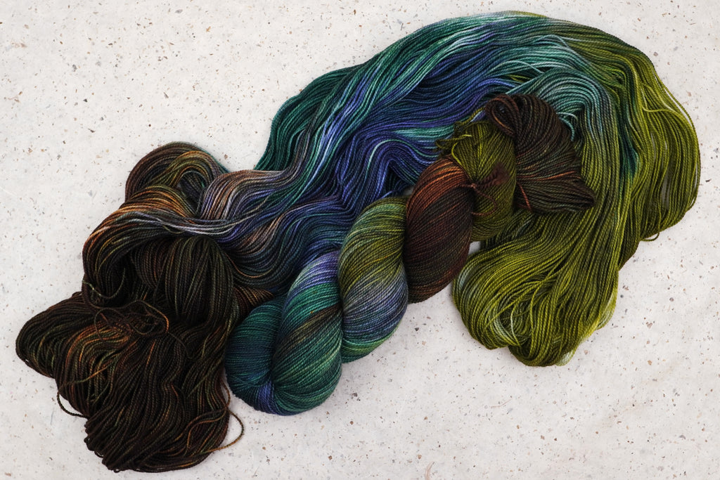 Fil Mycelium Bloom de Wild Woollys — un écheveau déroulé aux tons vert olive, brun foncé et bleu canard profond