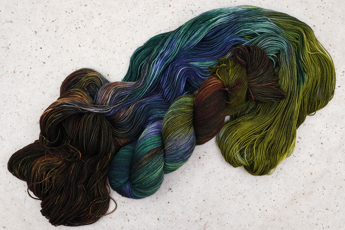 Wild Woollys Mycelium Bloom yarn, an unwound skein showing olive green, dark brown, and deep teal
