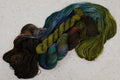 Kit chaussettes Mycelium Bloom de Wild Woollys — un écheveau déroulé aux tons vert olive, brun foncé et bleu canard profond avec une mini-pelote contrastante doré olive