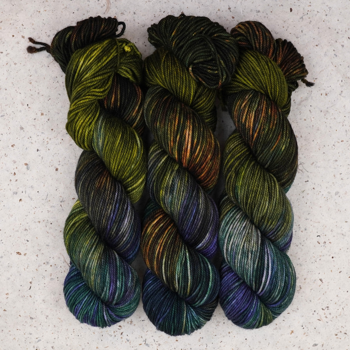 Wild Woollys Mycelium Bloom DK yarn, three skeins in olive green, dark brown, and deep teal