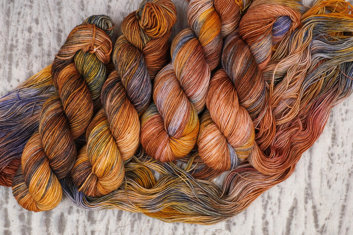 Wild Woollys Smashing Gourds yarn, twisted skeins resting on an unwound hank, in pumpkin orange, gold, and copper with speckles