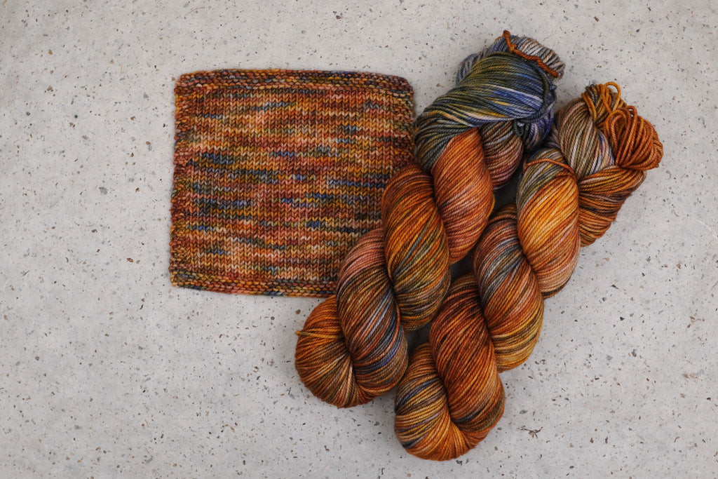 Wild Woollys Smashing Gourds yarn in rust orange, gold and blue, two skeins with a knitted swatch