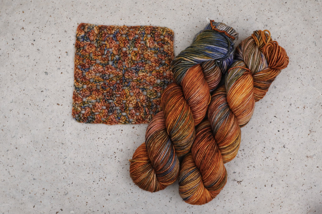 Wild Woollys Smashing Gourds yarn in rust orange, gold and blue, two skeins with a crocheted swatch