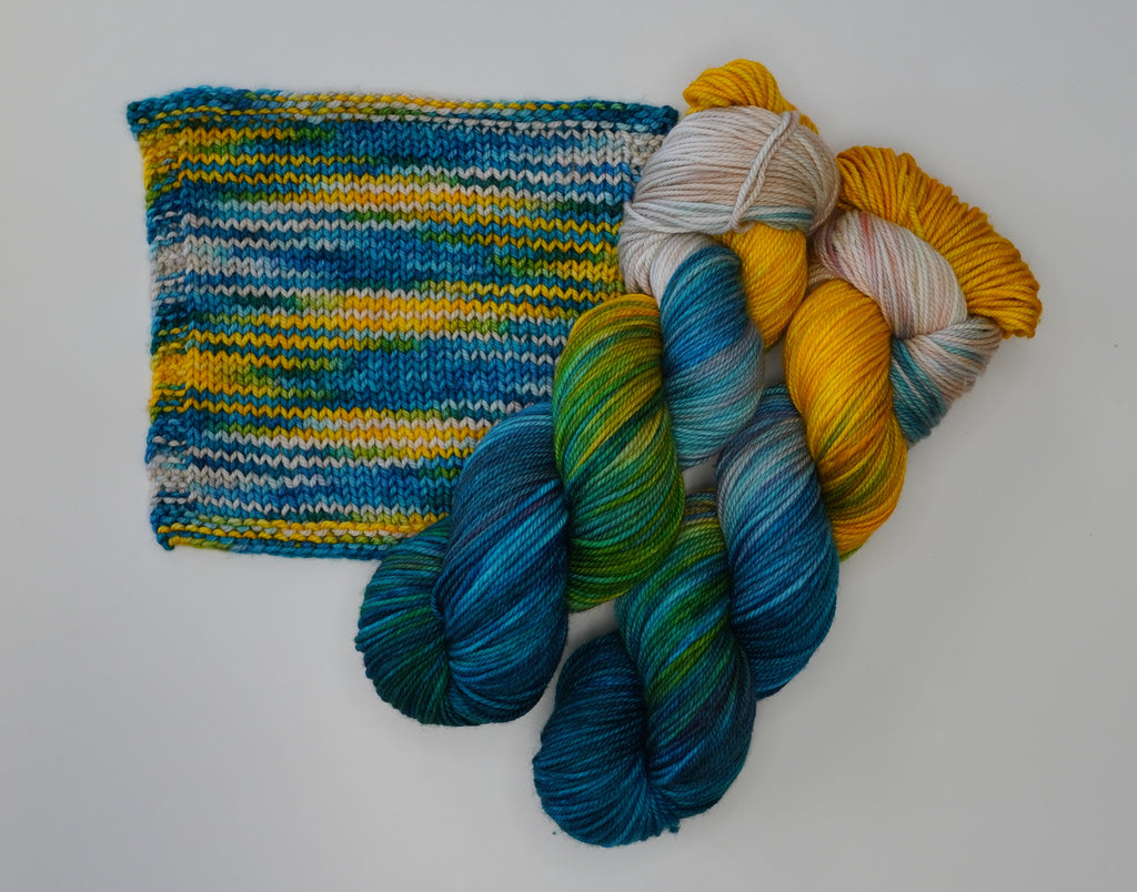 Tropical Escape yarn by Wild Woollys, a knitted swatch and three skeins of yarn in blue, green, and yellow