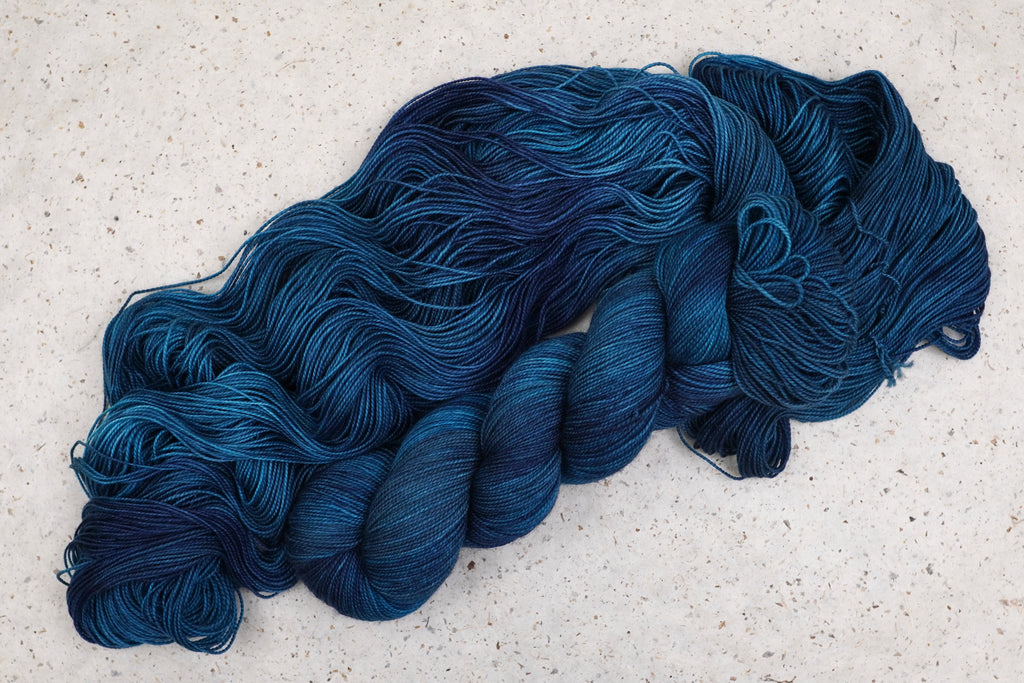 Wild Woollys Teal of Fortune yarn in deep teal and blue, twisted skeins resting on an open hank