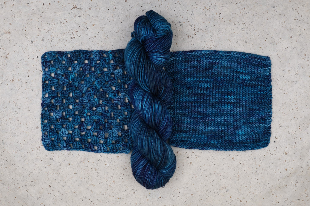 Wild Woollys Teal of Fortune yarn in deep teal and blue, one skein with knitted and crocheted swatches