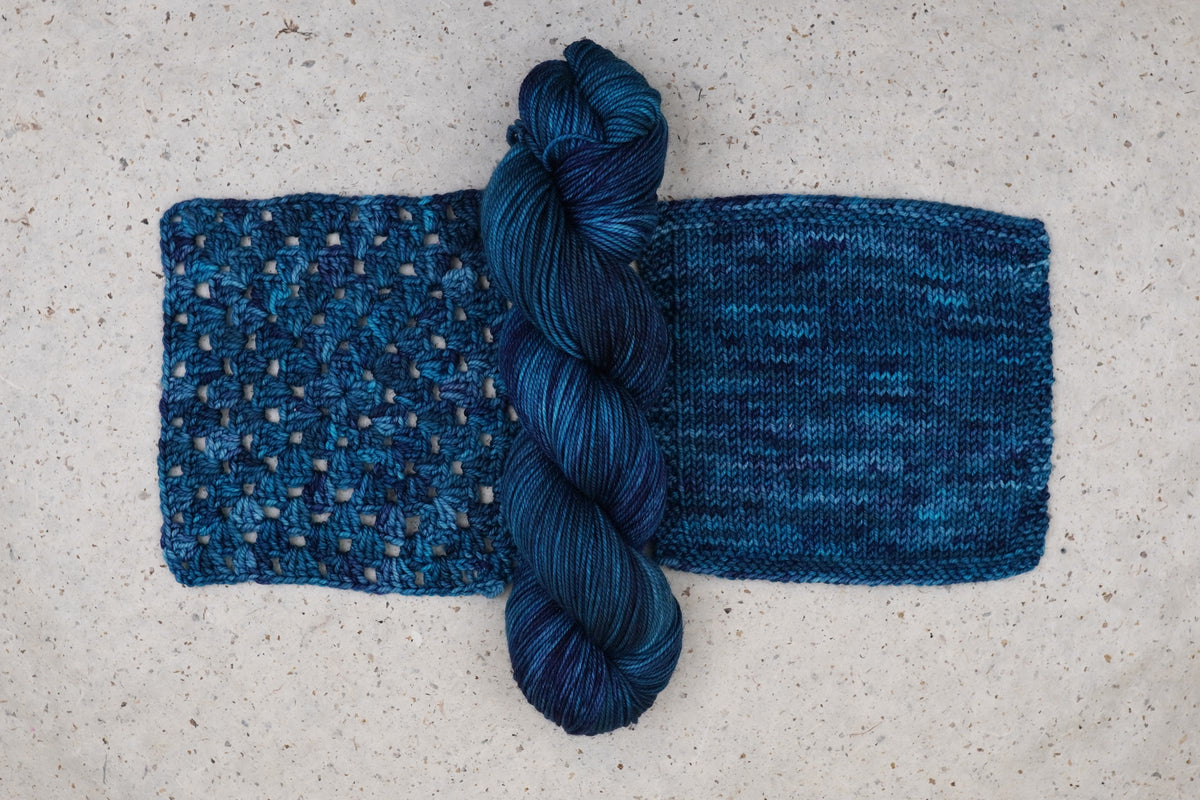 Wild Woollys Teal of Fortune yarn in deep teal and blue, one skein with knitted and crocheted swatches